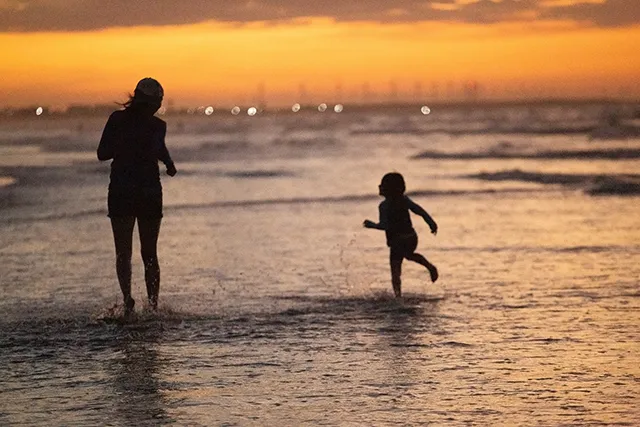 Pôr do sol em família nas praias de Luis Correia - Pousada Bellíssima Itália Silhuetas de adulto e criança brincando na beira do mar ao pôr do sol na praia de Luis Correia, Piauí.